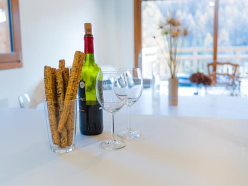 Bouteille de vin, verres et bâtonnets de pain aux graines sur table blanche avec vue sur les montagnes aux Tanières de Montgenèvre