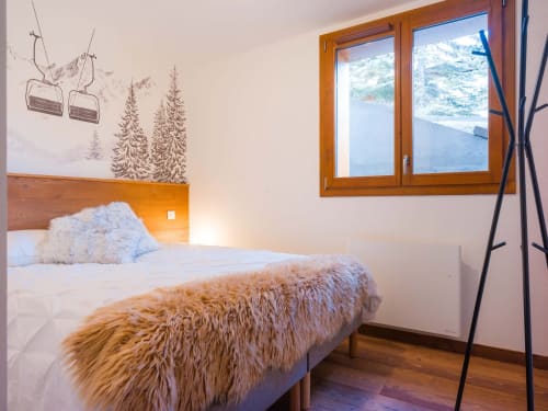 Chambre de montagne douillette avec tête de lit en bois, plaid moelleux, art mural télécabine, vue alpine enneigée