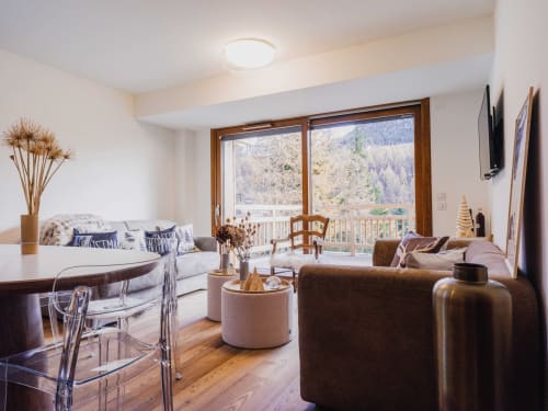 Salon d'appartement moderne en montagne avec canapé, fauteuil marron, mobilier en bois et vue panoramique sur les montagnes