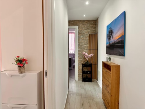 Moderno corridoio dell'appartamento di Loano con pavimento in legno, pareti bianche, fiori rosa, quadri paesaggistici e cassettone in legno