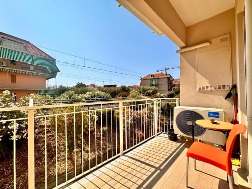Balcone soleggiato dell'appartamento di Loano con vista mare, climatizzatore e sedia arancione affacciati sui giardini
