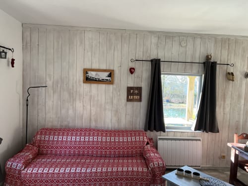 Séjour douillet avec canapé rouge à motifs, murs lambrissés, vue sur la piscine à LA JUMENT VERTE, Trévignin