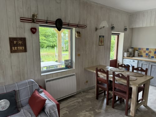 Coin repas du gîte avec table en bois, cuisine et grande fenêtre donnant sur les jardins de LA JUMENT VERTE, Trévignin
