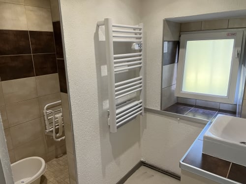 Salle de bain moderne du gîte LA JUMENT VERTE avec radiateur sèche-serviettes blanc, lavabo, douche et fenêtre dépolie à Trévignin, France