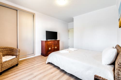 Spacious bedroom at Quinta do Águas villa in Lagoa with queen bed, wooden furniture, TV, and sliding wardrobe doors