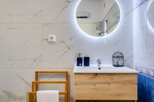 Modern bathroom at AlgarStays villa in Lagoa with marble walls, illuminated round mirror, wooden vanity, and blue decorative