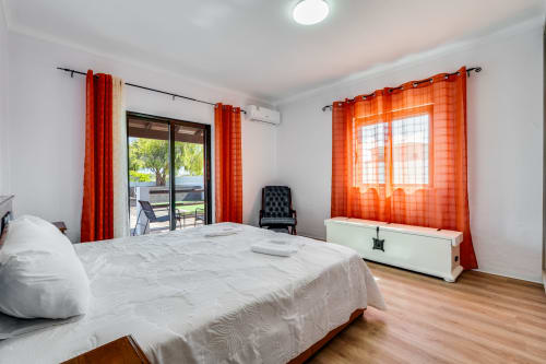 Bright bedroom with white bed, orange curtains, wooden floor, and terrace access at Quinta do Águas villa in Lagoa
