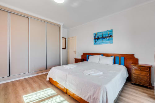 Spacious villa bedroom with wooden bed, blue pillows, modern wardrobe, and city skyline artwork at Quinta do Águas in Lagoa,