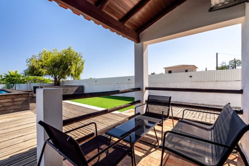 Covered terrace with black lounge chairs overlooking private pool and manicured green lawn at Quinta do Águas villa, Lagoa