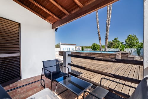 Covered terrace with wooden beams, lounge chair, and pool view at Quinta do Águas villa in Lagoa, Portugal