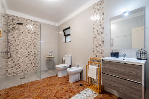 Modern bathroom at Quinta do Águas villa in Lagoa with walk-in shower, dual sinks, and terra cotta tile flooring.