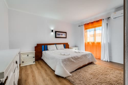 Bright bedroom at Quinta do Águas villa in Lagoa, Portugal, featuring wooden bed, white bedding, orange curtains, and