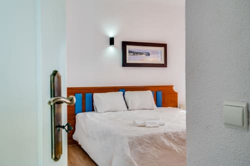 Modern bedroom with wooden bed frame, blue headboard cushions, white bedding, and wall sconce in Quinta do Águas villa, Lagoa