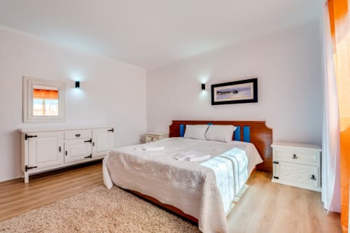 Spacious bedroom at Quinta do Águas villa in Lagoa with wooden bed, white furnishings, hardwood floors, and pool view framed