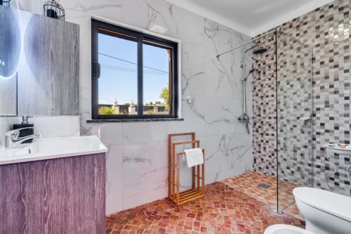Modern bathroom with marble walls, purple vanity, mosaic tile shower, and window overlooking Lagoa at AlgarStays villa