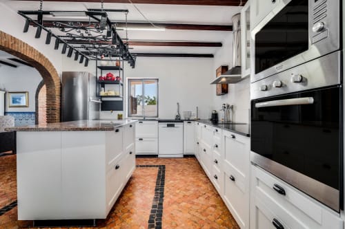Modern kitchen with white cabinets, stainless steel appliances, terracotta tile floor, and exposed wooden beams at Quinta do