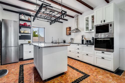 Modern white kitchen with stainless appliances, island counter, and terra cotta tile flooring at Quinta do Águas villa in
