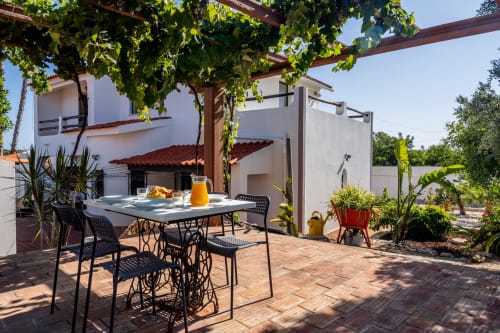 Outdoor patio at Quinta do Águas villa in Lagoa with dining table, pergola, lush greenery, and white architecture.