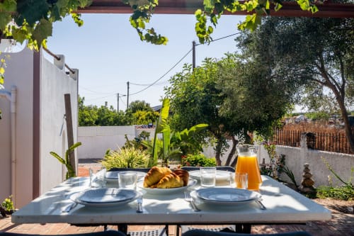 Outdoor dining table set for breakfast on a sunny patio at Quinta do Águas villa in Lagoa, Portugal, with garden views and