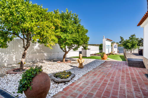 Sunny courtyard at AlgarStays villa in Lagoa with terracotta patio, green trees, white buildings, and decorative garden