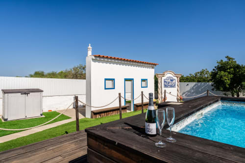 White villa with blue-trimmed windows, private pool, champagne and glasses on wooden table at Quinta do Águas in Lagoa,