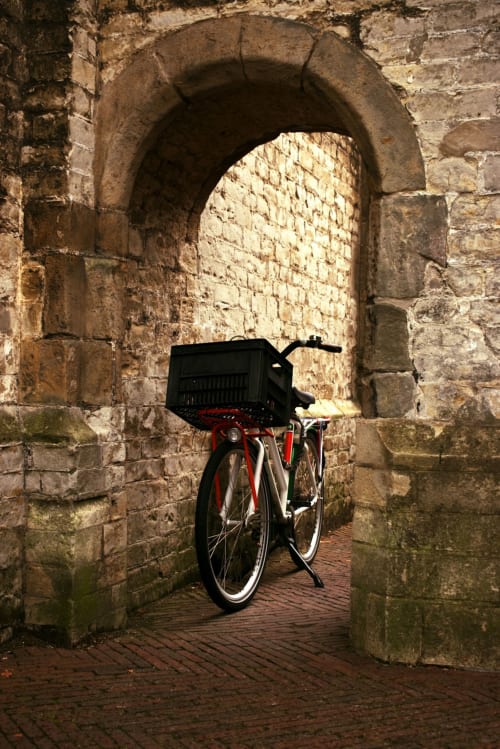 Red bicycle with black basket in stone archway at Aldea Rural Pazos De Arenteiro, Spain