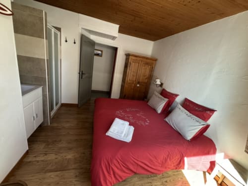 Chambre spacieuse avec literie rouge au gîte LA JUMENT VERTE à Trévignin, plafond en bois et salle d'eau attenante
