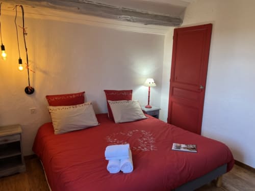 Chambre douillette à LA JUMENT VERTE avec literie rouge, oreillers blancs, lampe de chevet et porte assortie