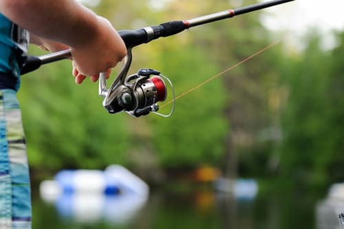 Person holding fishing rod with reel by river at Aldea Rural Pazos De Arenteiro