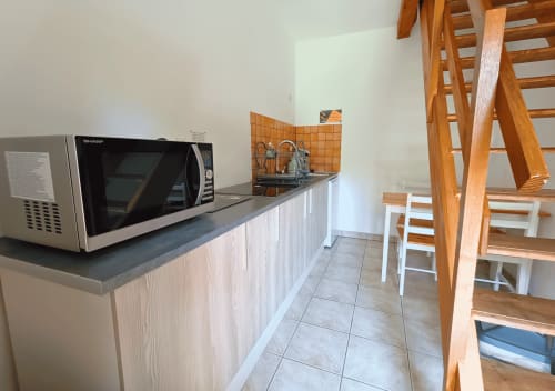 Studio kitchenette met magnetron, gootsteen, witte kasten, tegelvloer en houten trap bij La Synchronicité BnB