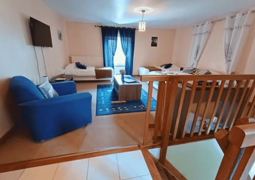 Studio de l'Écureuil in La Synchronicité B&B: Helder woongedeelte met blauwe fauteuil, houten meubels, bedden en tuinuitzicht
