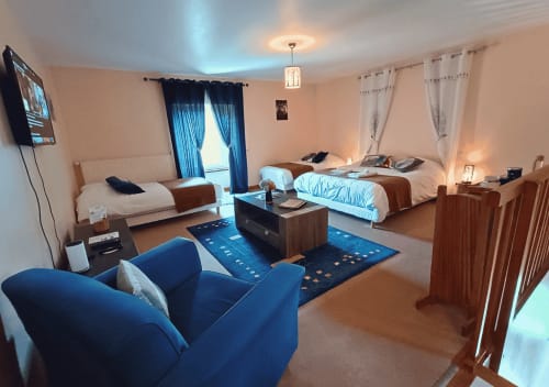 Studio de l'Écureuil in La Synchronicité BnB: ruim ingerichte kamer met twee bedden, blauwe fauteuil, TV en tuinuitzicht