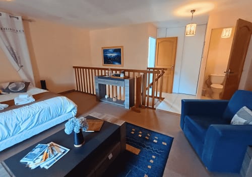 Eekhoorn Studio in La Synchronicité B&B: ruime kamer met bed, blauwe fauteuil, kitchenette en houten loftruimte.