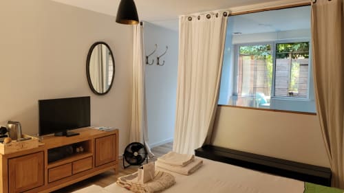 Dormitorio moderno en Le Lodge du Cap Ferret con muebles de madera, TV, ventana con vista al jardín y cortinas color crema en la habitación Urban Mood