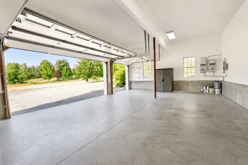 Spacious modern garage with open doors showing manicured grounds, concrete floor, and amenities at Malkita Aria villa in