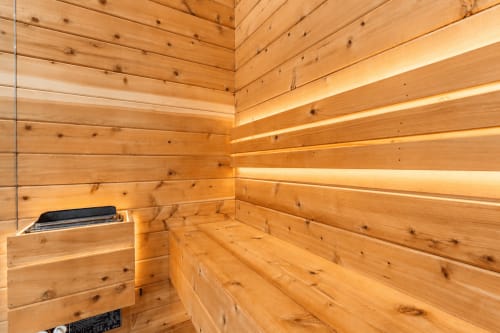 Wooden sauna interior at Malkita Aria with built-in benches, ambient lighting, and modern heater in Woodbury villa