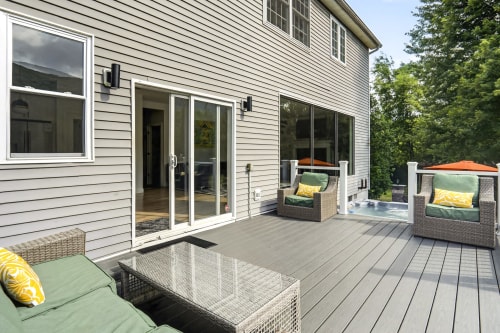Modern gray deck with wicker furniture, green cushions, orange umbrellas, and glass table at Malkita Aria villa in Woodbury