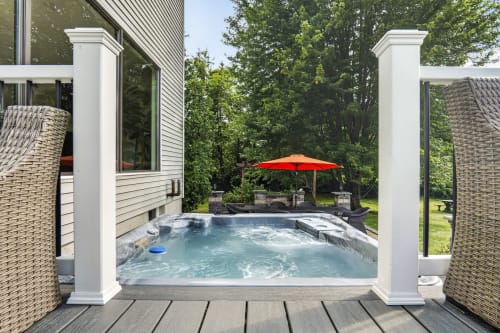 Malkita Aria villa in Woodbury features a steaming private hot tub on a wooden deck with white columns, red umbrella, and