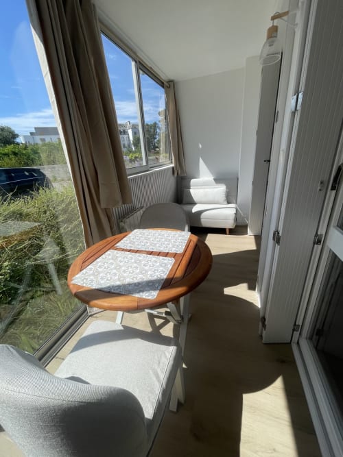 Studio lumineux à Guimiliau avec table en bois, sièges confortables et grandes fenêtres sur paysage verdoyant