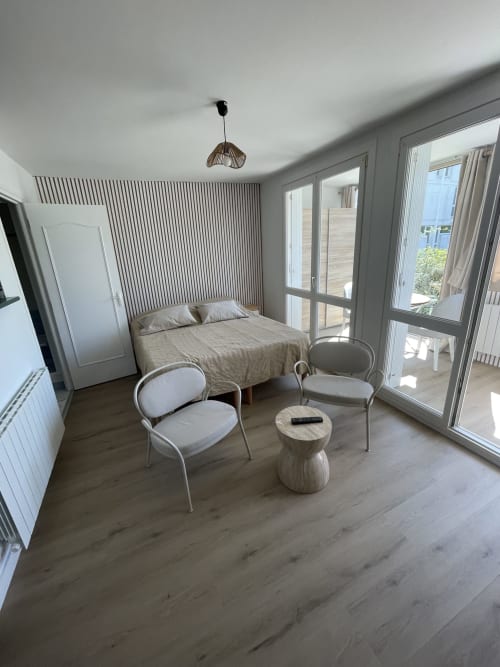 Chambre de studio moderne avec lit, coin détente et portes vitrées ouvrant sur balcon à Guimiliau, France