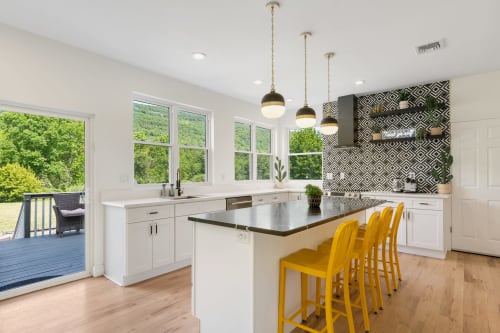Modern kitchen with white cabinetry, black countertop island, yellow bar stools, pendant lights, and views of forested
