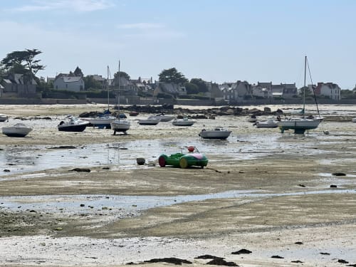 Voiture de course verte vintage sur la plage de Roscoff à marée basse, avec voiliers amarrés et bâtiments historiques du front de mer, Bretagne France