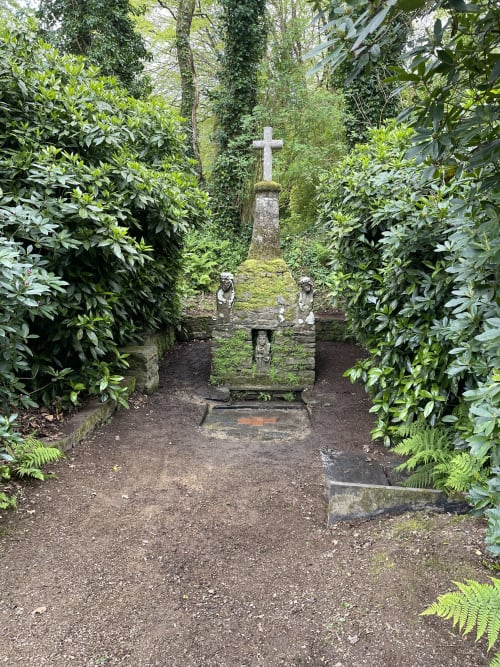 Croix de pierre dans un cimetière envahi par la végétation luxuriante et les arbres couverts de lierre à Guimiliau, Bretagne