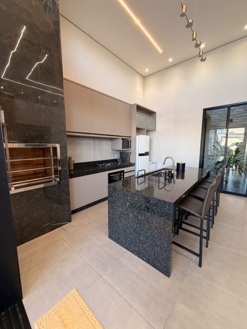 Cozinha moderna com ilha de mármore negro, eletrodomésticos em aço inoxidável e bar na Casa Coqueiros em Maringá