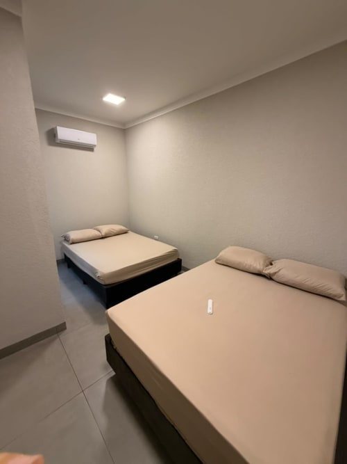 Dois leitos gêmeos com roupas de cama bege em um quarto minimalista e aconchegante na pousada Estadia e Alegria em Maringá