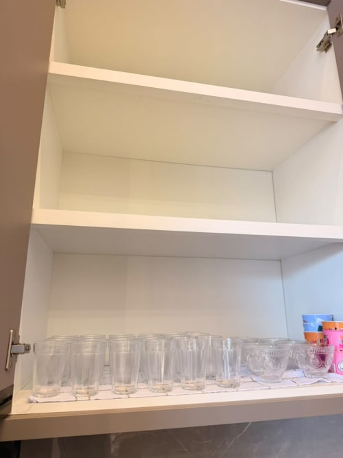 Armários brancos da cozinha com copos e recipientes de vidro vazios na pousada Casa Coqueiros em Maringá