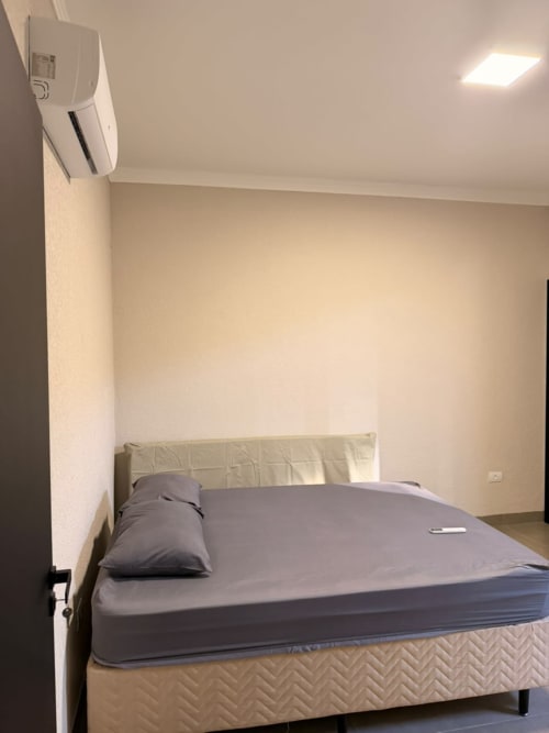 Quarto moderno com cama queen, roupa de cama cinza, cabeceira creme e ar condicionado na pousada Casa Coqueiros em Estadia