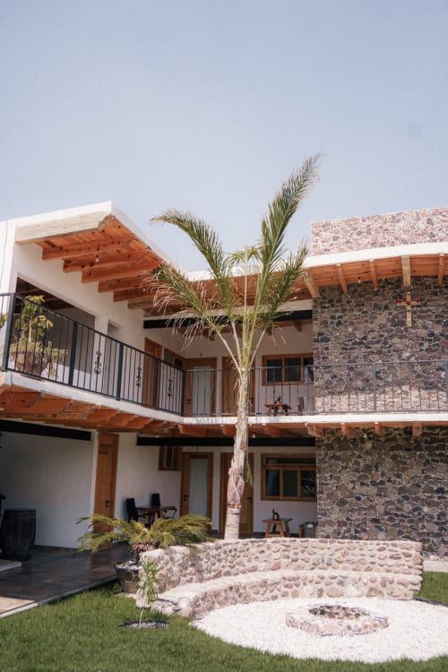 Patio contemporáneo del Hotel El Porvenir en Querétaro con arquitectura de piedra, vigas de madera, palmeras y terrazas