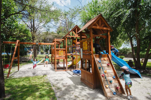 Parque infantil de madera con tobogán y estructuras para trepar en la villa Hotel El Porvenir en Querétaro, rodeado de árboles y vegetación verde