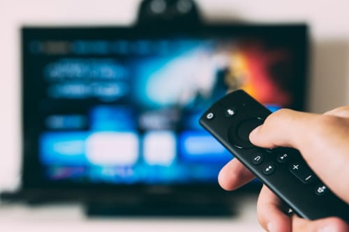Mão segurando controlo remoto apontado para TV com sistema de streaming de entretenimento na AgapeStay Porto